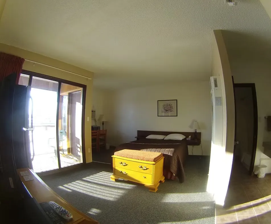 Spacious bedroom with bed, yellow chest, and sunny balcony