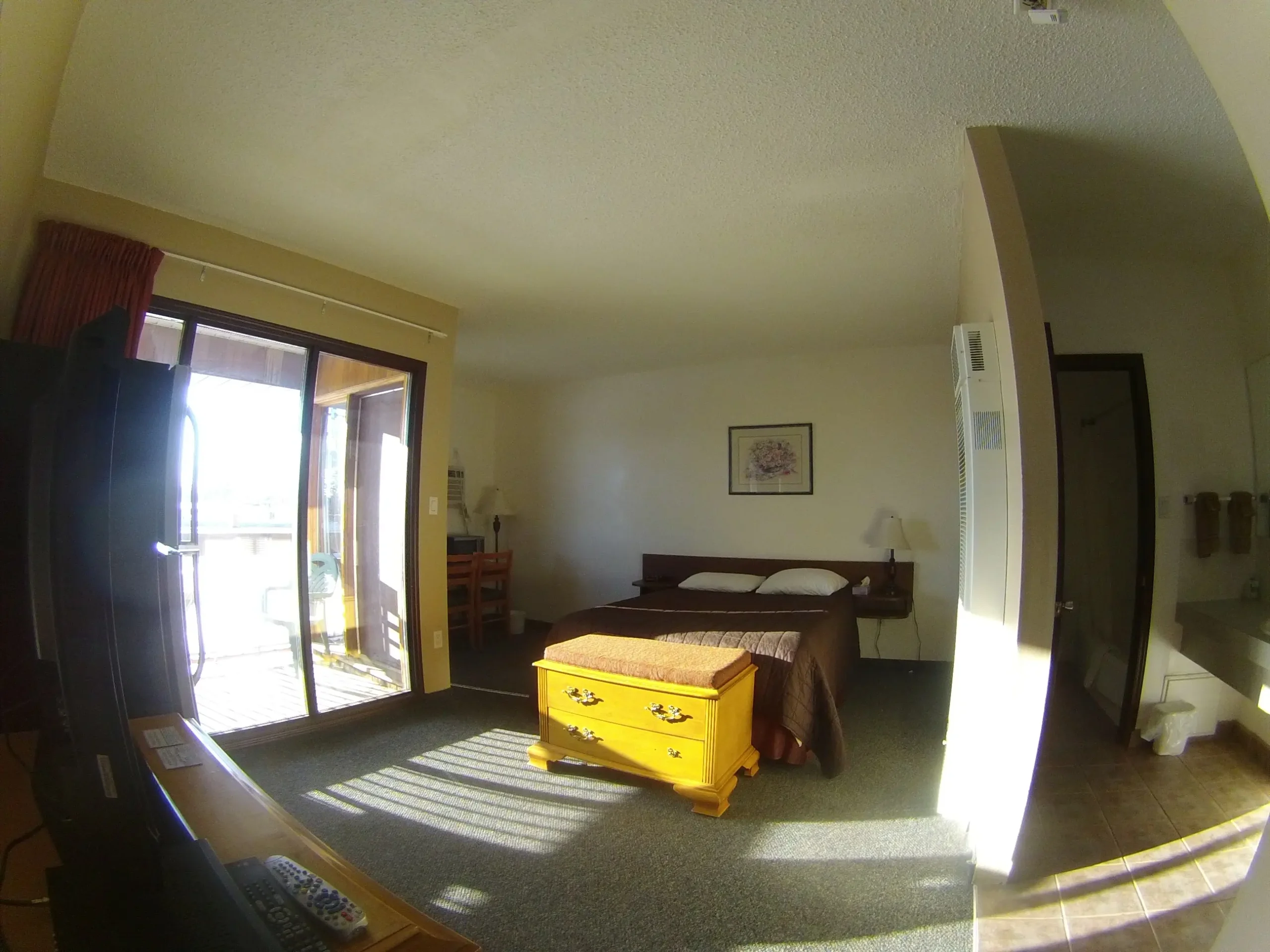Spacious bedroom with bed, yellow chest, and sunny balcony