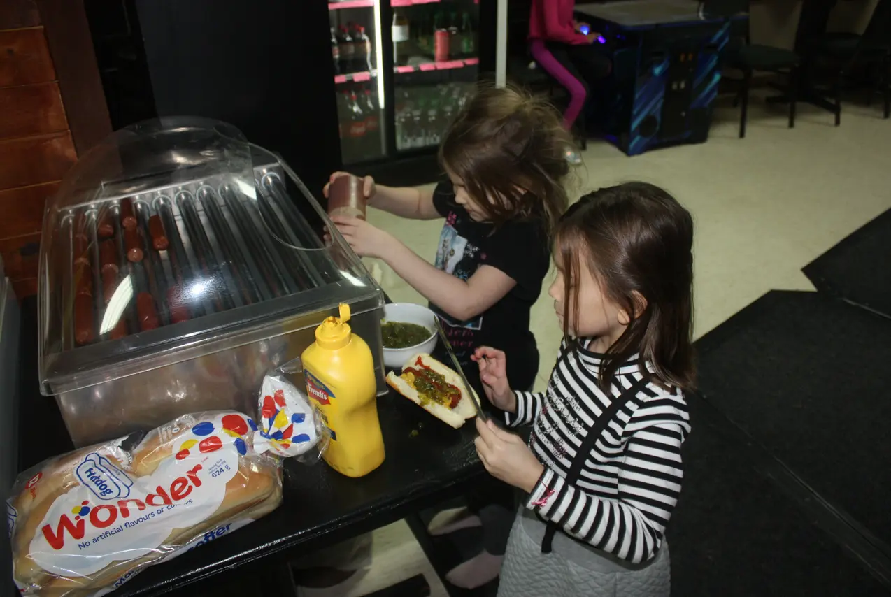 Two girls preparing hot dogs, adding ketchup